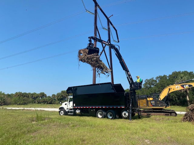 Grapple truck hoists debris beneath transmission lines