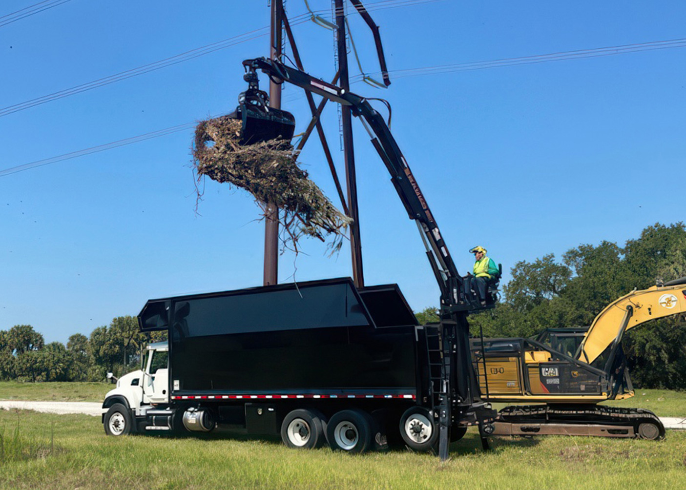 Kubota loader and bucket truck handling heavy limbs near a roofline