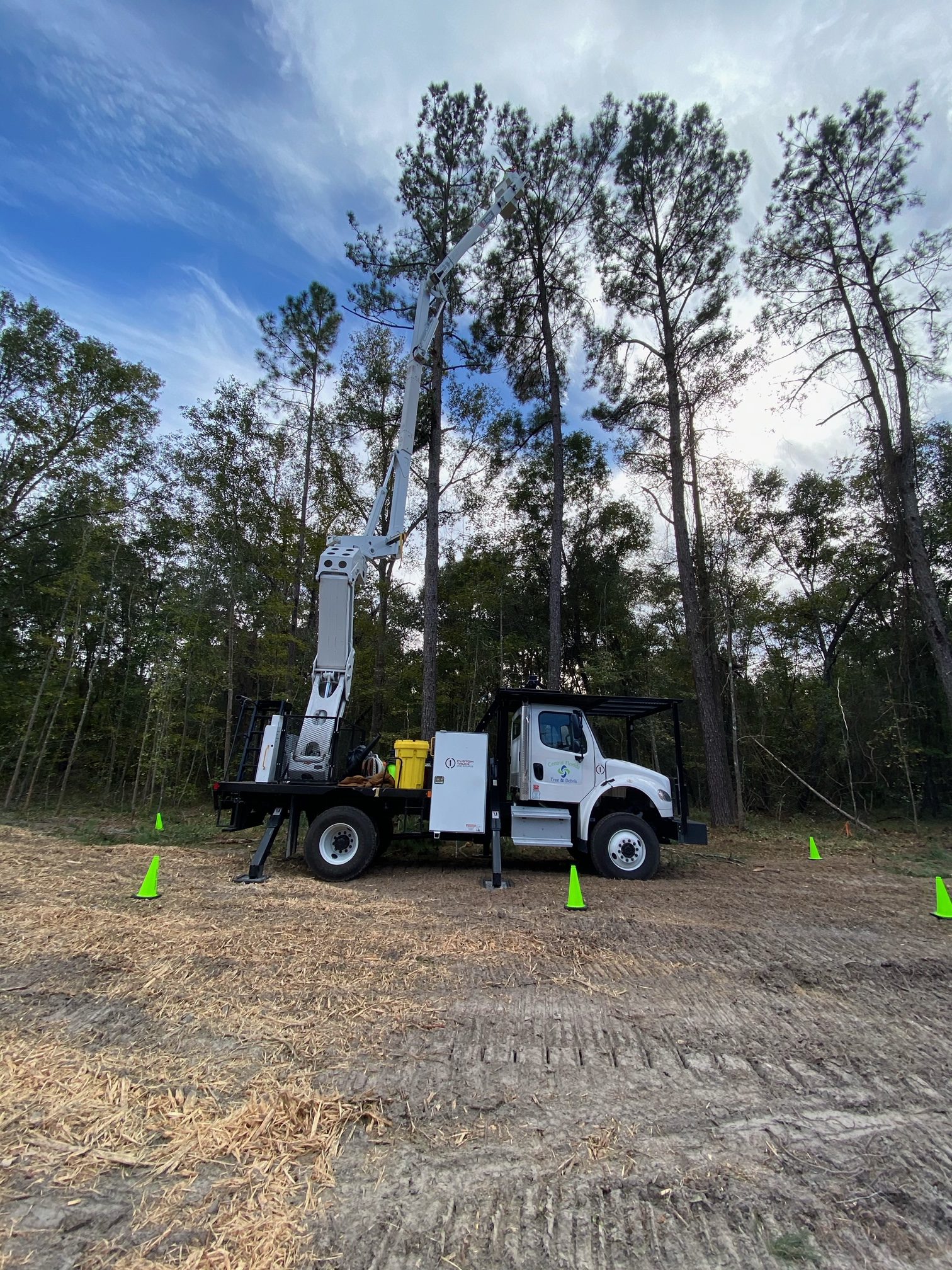 Bucket trucks with crews trimming roadside trees under safety cones